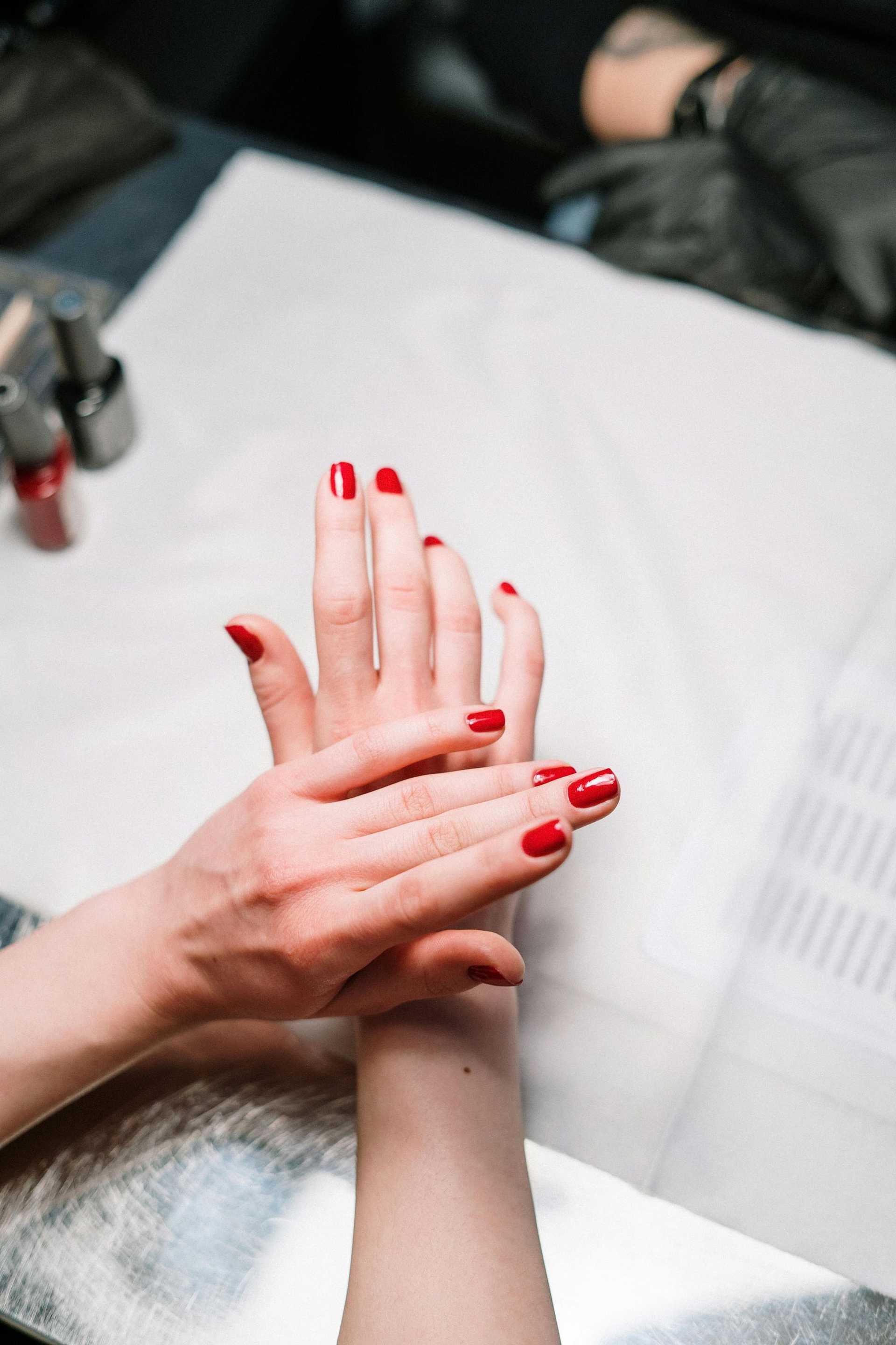 Nail technician applying red polish to a client's nails at a salon.
