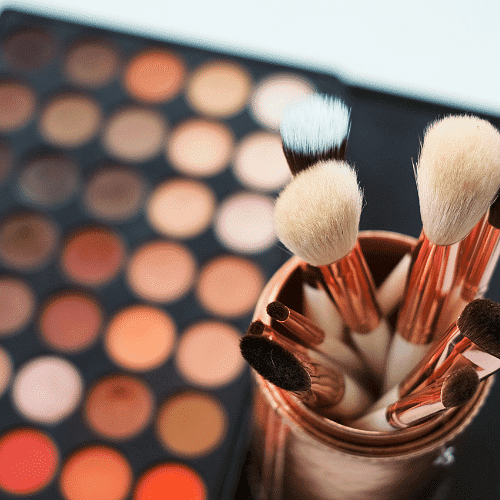 Makeup brushes in a holder with a blurred palette in the background.